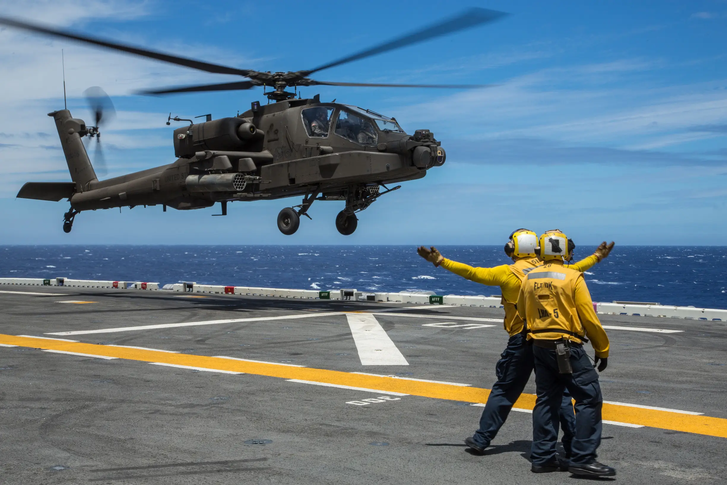 AH-64E Apache landing on the flight deck of USS Peleliu while sailors signal it down